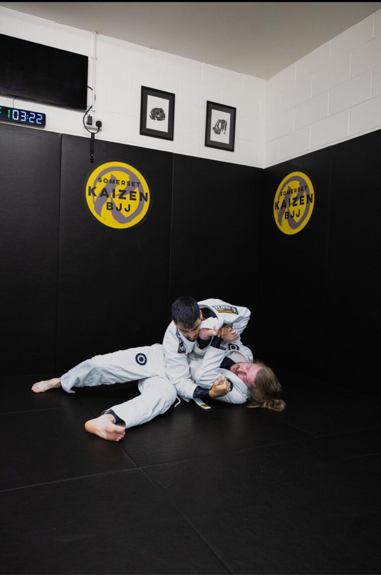 Students spar in front of the Kaizen BJJ wall logo.