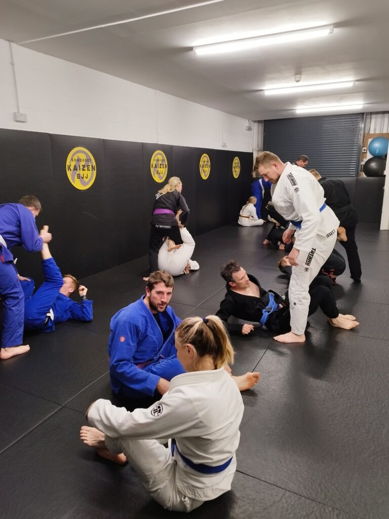 A coach demonstrates a jiu-jitsu technique as students practise in pairs.